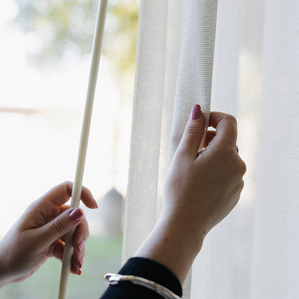 Hands adjusting sheer white curtains with a wand